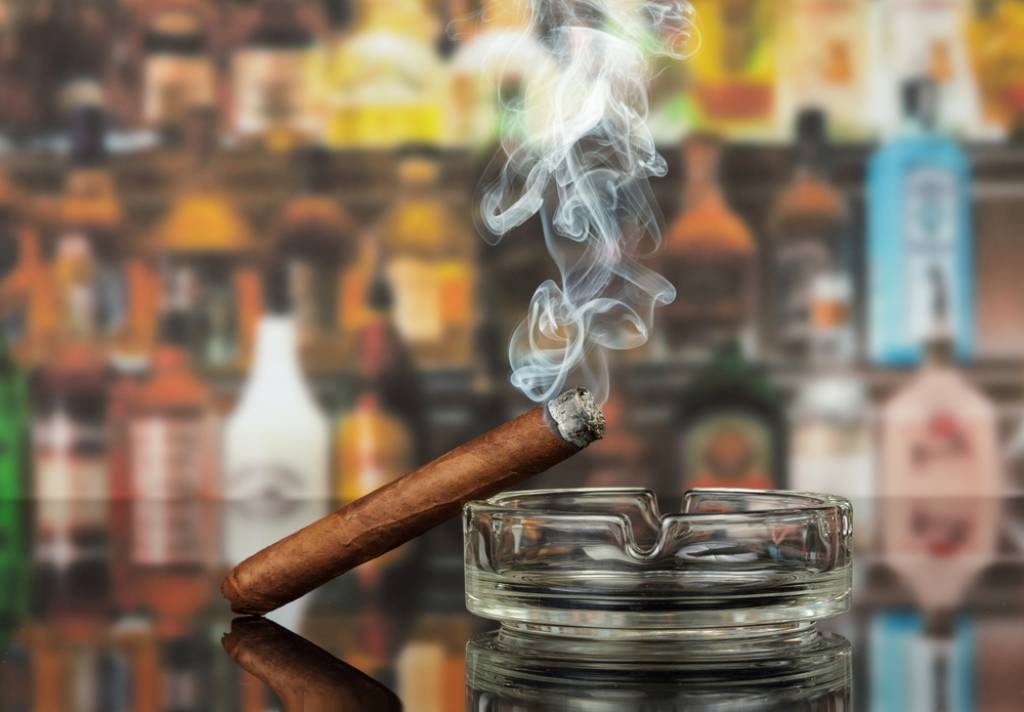 Smoking cigar leaning on an ashtray with a bar in the background