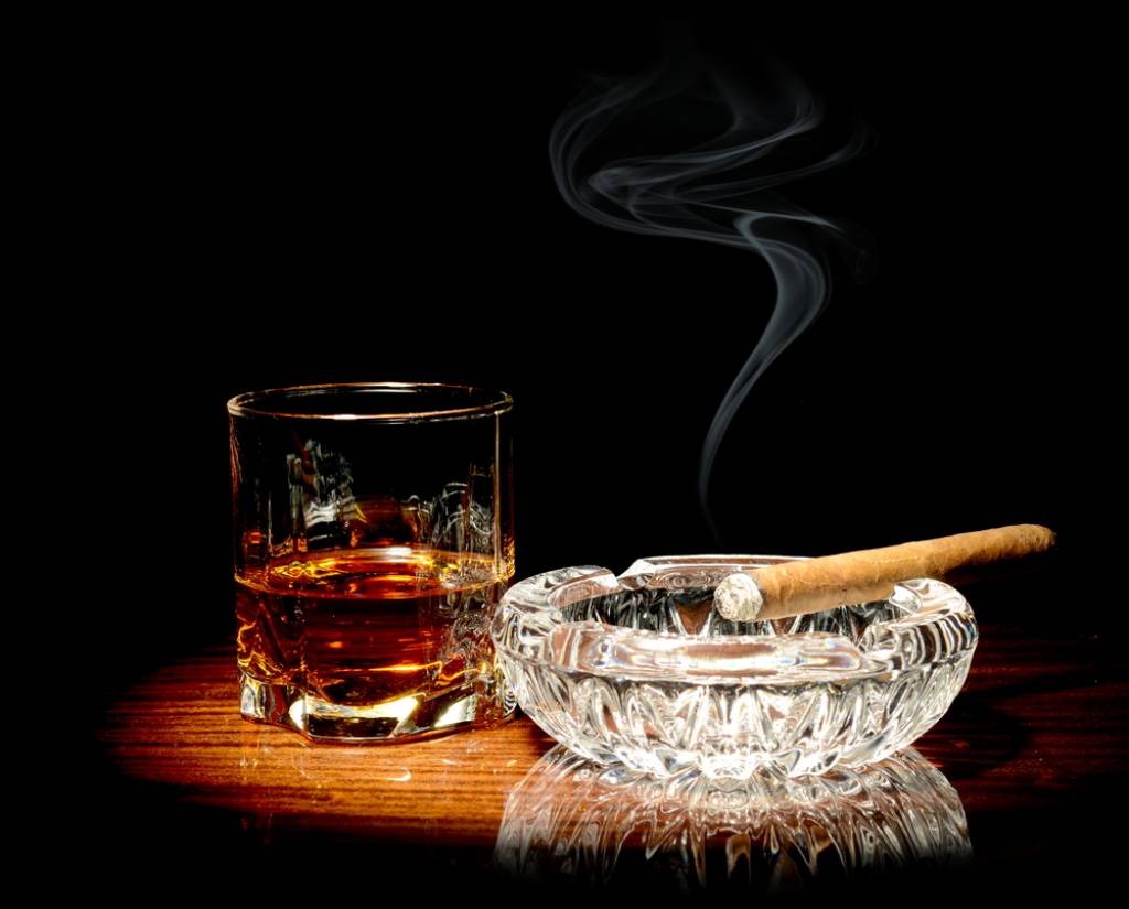 A cigar resting on an ashtray next to a glass of whiskey