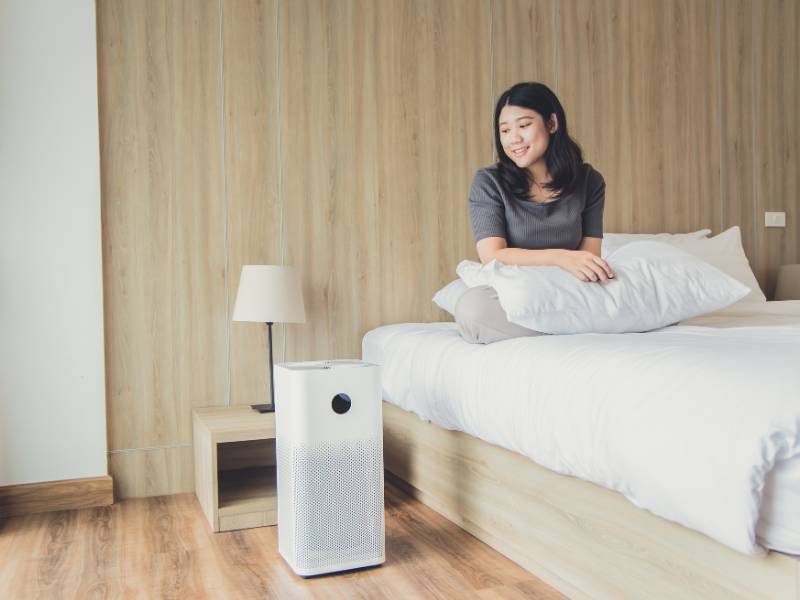 A woman in bed looking at her portable HEPA air purifier