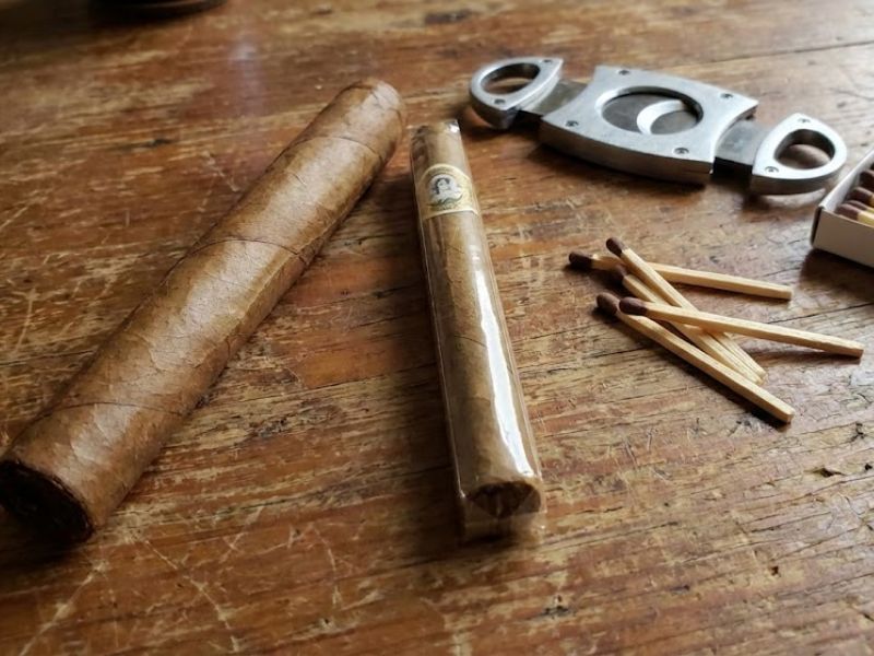 A cigar next to a cigarillo on a wooden table