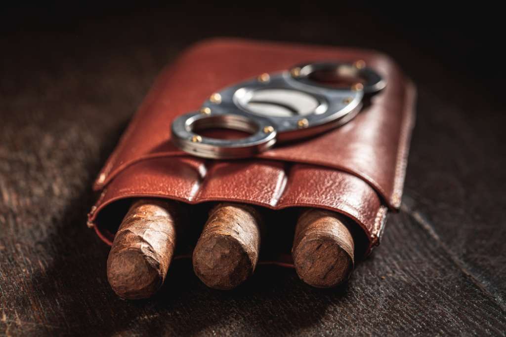 Three cigars in a leather case with a cigar cutter on top