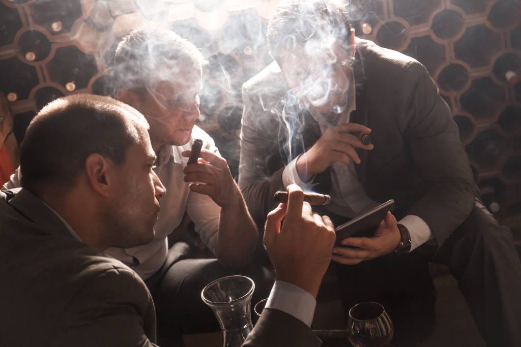 Three men smoking cigars while socializing in a lounge.